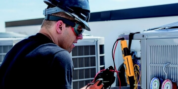 Technician wearing safety gear providing maintenance services to HVAC equipment. 